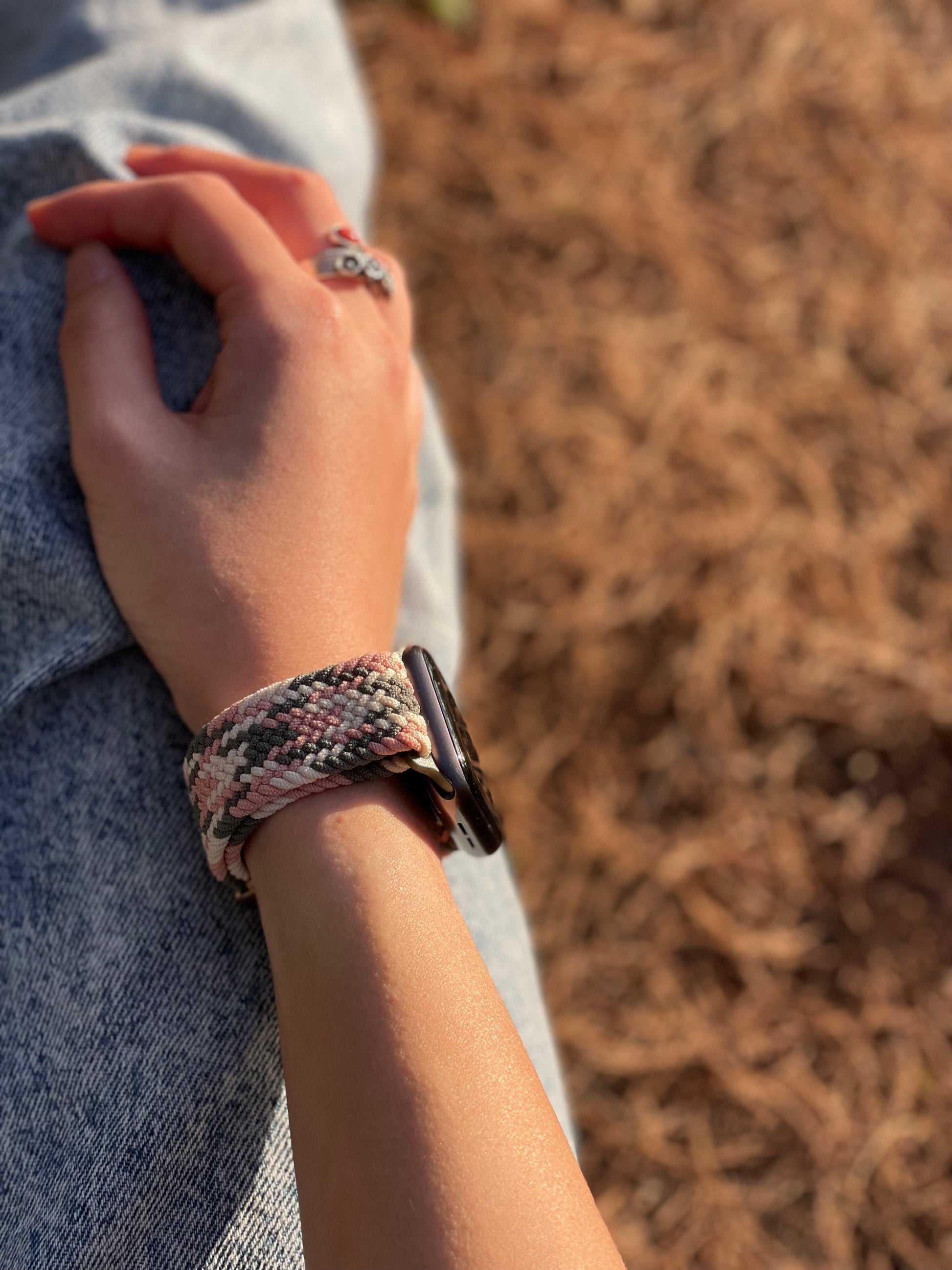 Hand wearing a green-and-pink apple watch band with a blurred natural background
